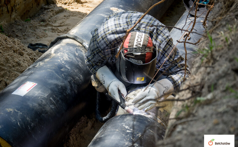 mężczyzna w kasku spawający rury ciepłownicze